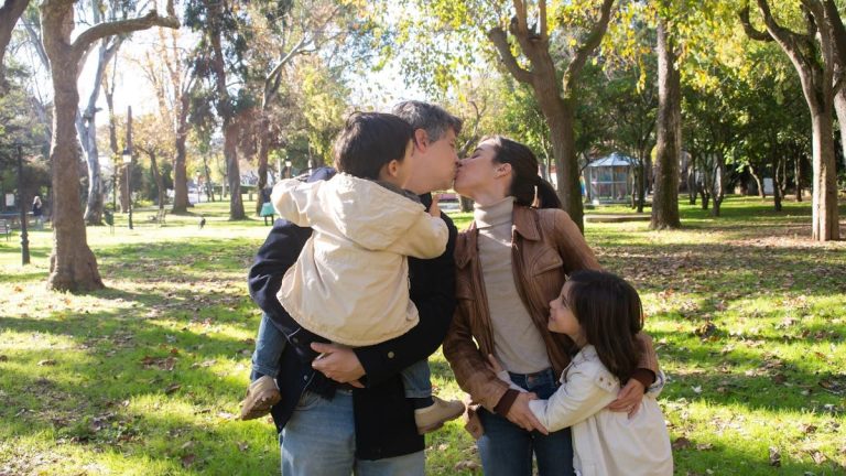 A joyful family sharing a tender moment in a sunny park setting.
